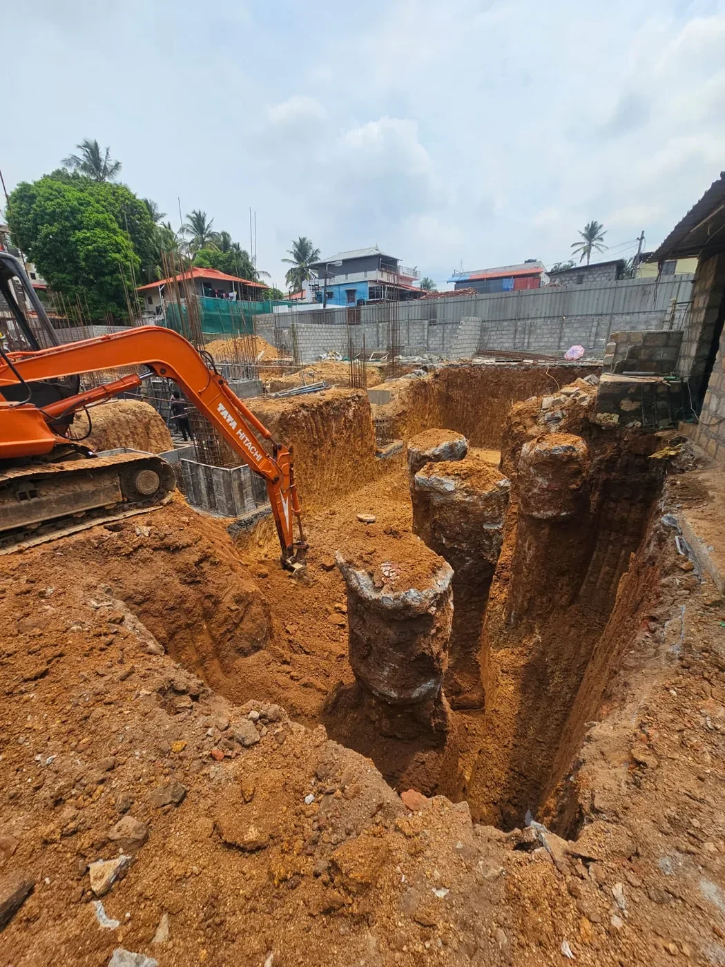 Excavator digging a deep foundation trench at a construction site.
